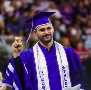A student athlete gives a "Go Frogs" hand sign as he walks across the stage at TCU Commencement.