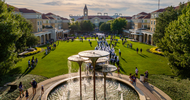Students gather in the Campus Commons with Frog Fountain in the foreground and the tops of Amon G. Carter stadium peeking above the rooftops in the background